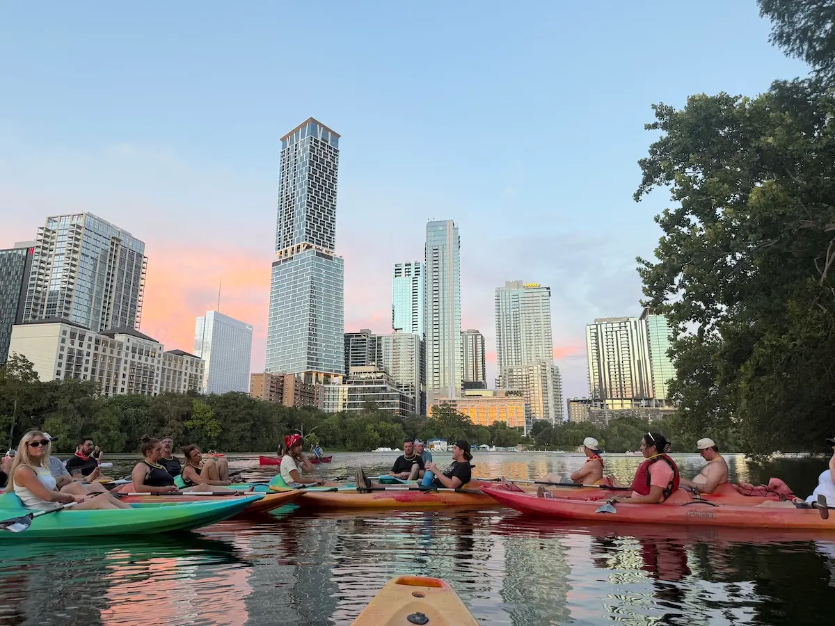 Group of kayakers gathered on Lady Bird Lake with the Austin skyline glowing at sunset